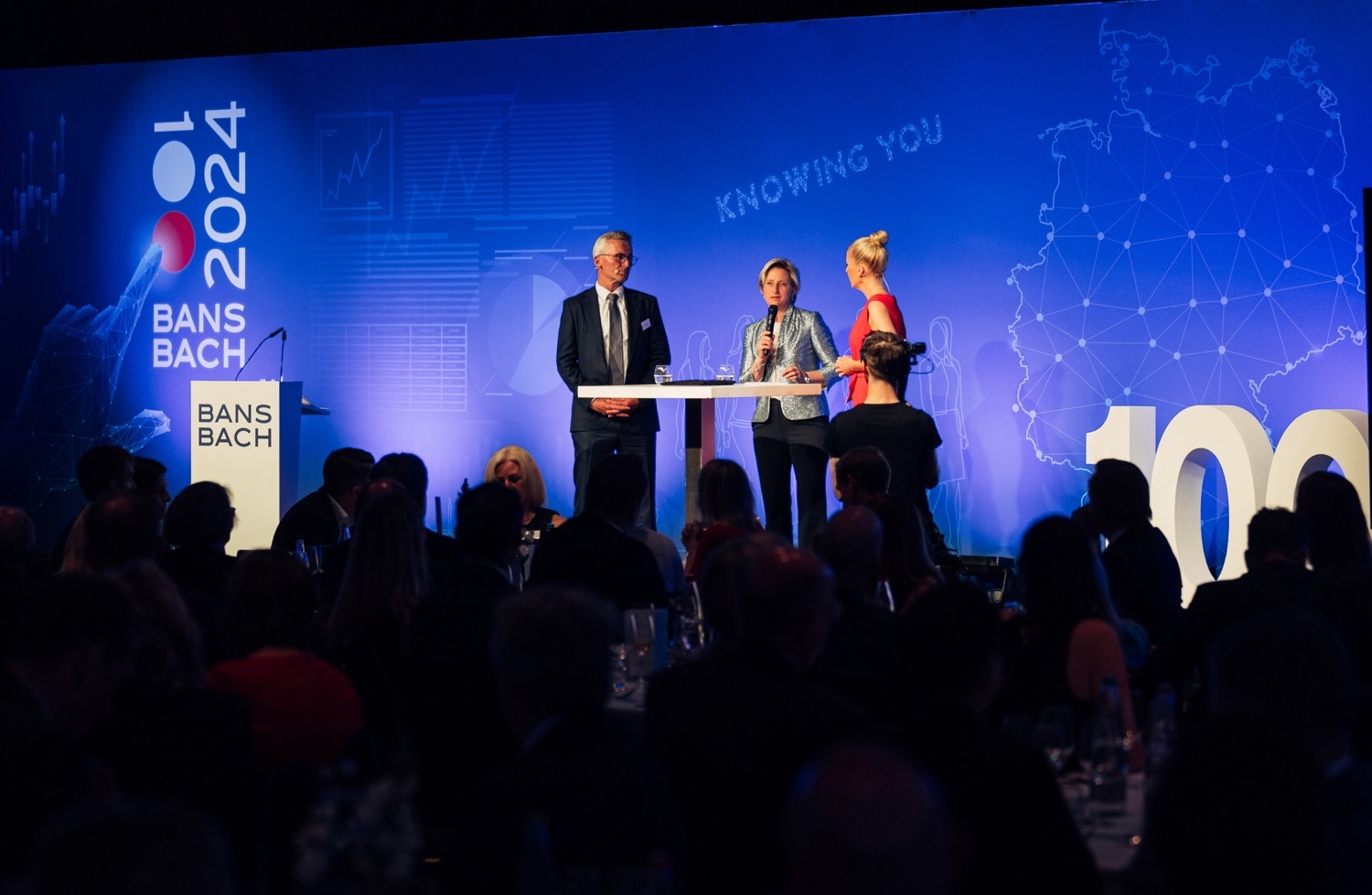 Moderatorin und zwei Sprecher auf der Bühne der 100 Jahre BANSBACH Jubiläumsgala in Stuttgart